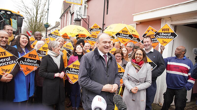 Ed Davey with laughing crowd holding Liberal Democrat diamond signs