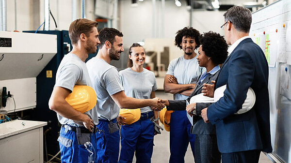 Fix Britain's Trade A group of workers in a factory. Two people are shaking hands.
