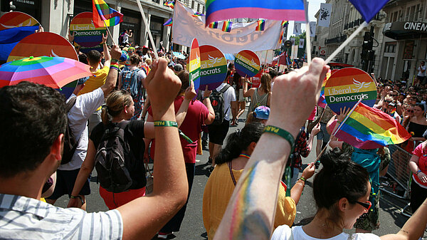 Pride A Liberal Democrat group at Pride. The people are walking away from the camera, they are holding Lib Dem rainbow signs.