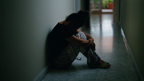 A woman sat in an empty corridor with her head in her knees