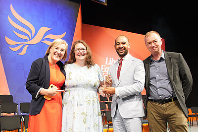 Josh Babarinde MP presenting a Party Award on the Conference stage alongside MPs Lisa Smart and Tim Farron