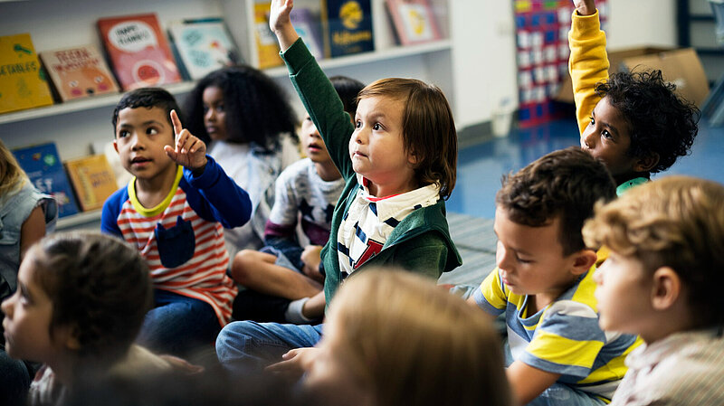 Young happy children sat on the floor at school with hands raised