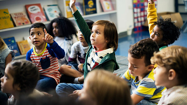 Young happy children sat on the floor at school with hands raised