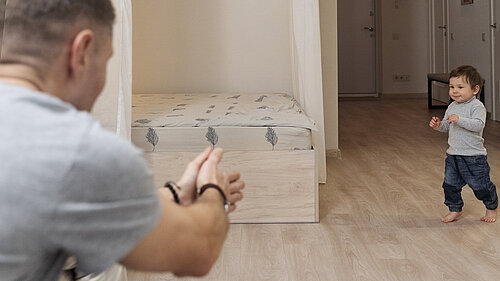 A child runs towards their parent in an empty bedroom