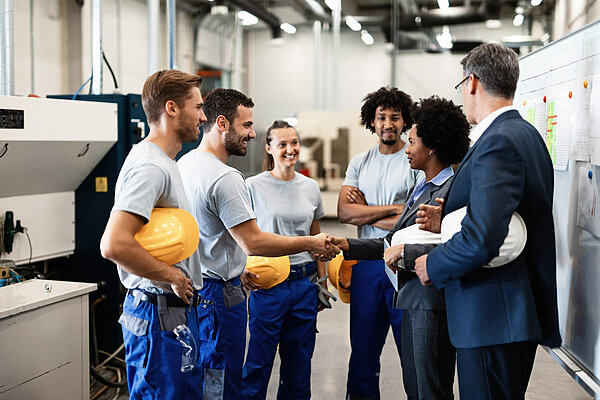 A group of workers in a factory. Two people are shaking hands.