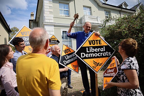Ed Davey hammering in a garden poster