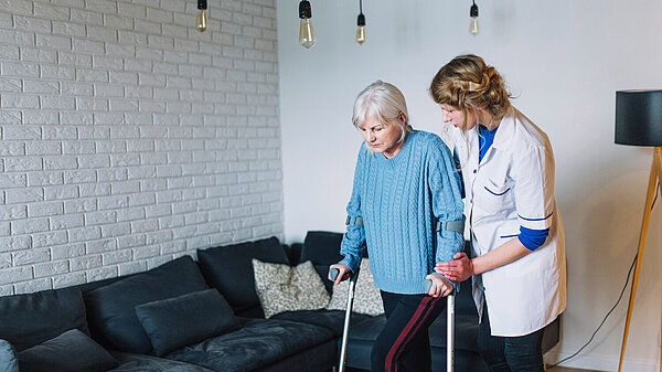 Carer helping older person on crutches