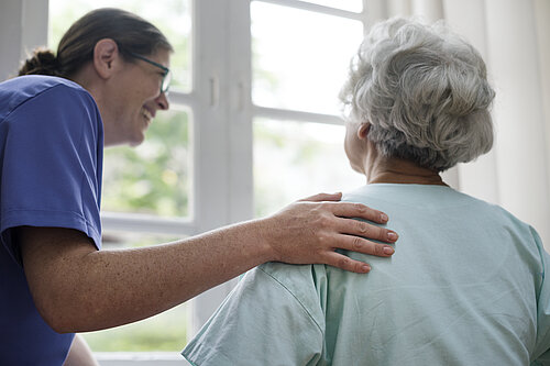 A carer helps an elderly woman to stand