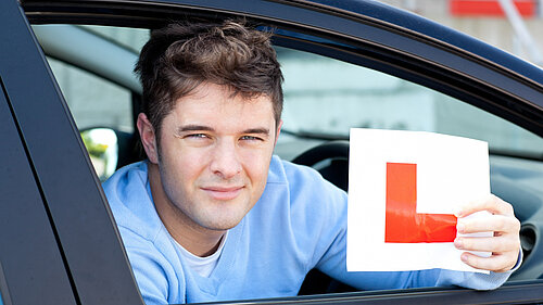 Person sat in a car holding up an L-plate
