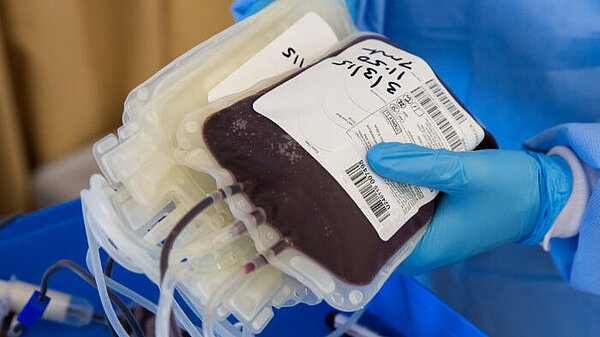 A person in scrubs and medical gloves holding a bag of donated blood