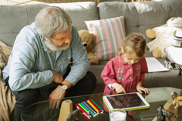Older man watches child playing on a tablet