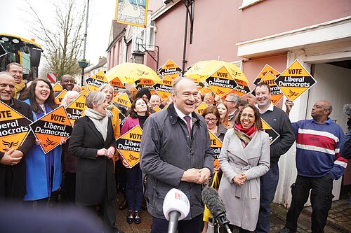 Ed Davey with laughing crowd holding Liberal Democrat diamond signs