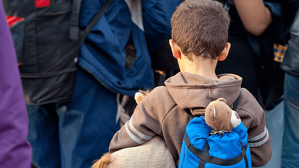 A child refugee with a stuffed toy walks away