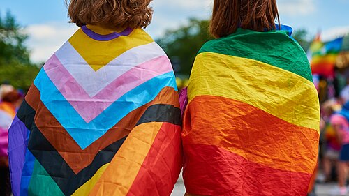 two women with LGBT flags draped over their shoulders