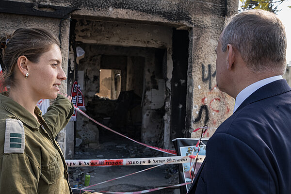Ed Davey speaks to a woman in uniform, in the background is a burnt-out house at the Kfar Aza kibbutz which was attacked by Hamas on 7 October 2023