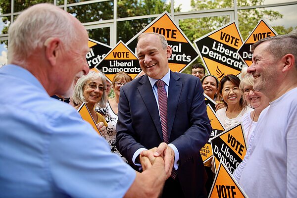 Ed Davey shakes hands with a man in front of a crowd holding Lib Dem signs