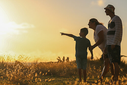 A child and two adults look at a sunset
