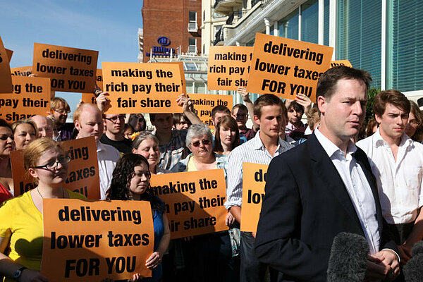 Nick Clegg speaks in front of a crowd holding sings campaigning for fairer taxes
