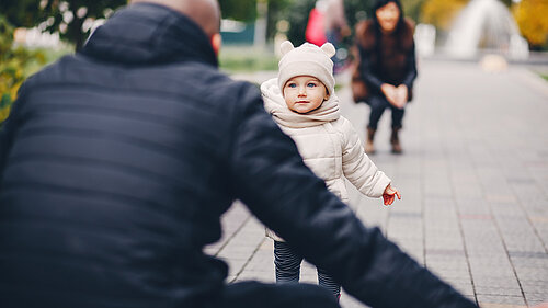 Man facing away from the camera with arms open as child runs towards him