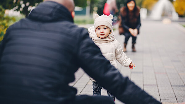 Man facing away from the camera with arms open as child runs towards him