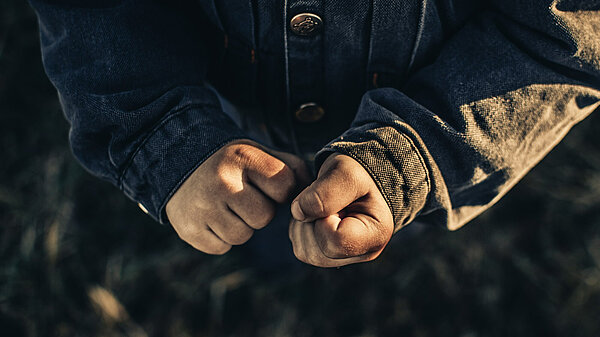 Small hands clasped in fists, wearing brown coat