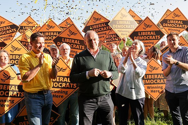 Ed Davey and the Liberal Democrats celebrate local election wins. Ed Davey, Charlie Maynard, Olly Glover and Liz Leffman stand in front of a crowd with Lib Dem diamond signs as golden confetti rains down.