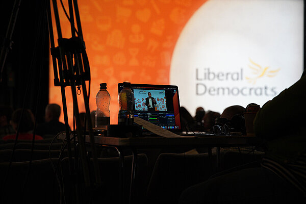 A camera monitor in the foreground shows Tim Farron, in the background is the Liberal Democrats logo as part of the conference set.