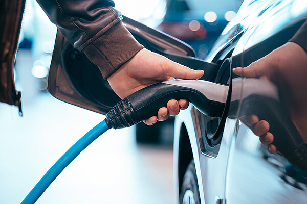 Human hand holding an electric car charging connector to electric car