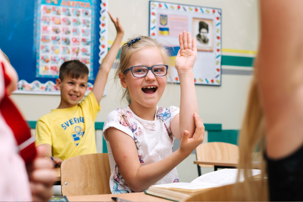 Children in a SEND classroom, engaging with the lesson. Focal point of the picture is a young girl in glasses, having fun.